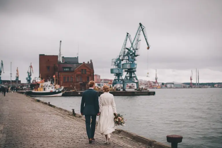 Brudpar som promenerar längs Göteborgs hamnstråk med industrikajer i bakgrunden