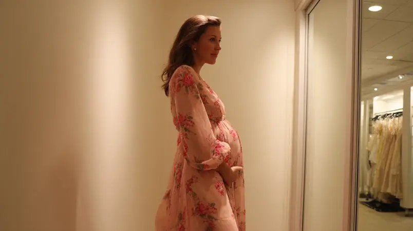 Gravid kvinna i andra trimestern provar klänning framför spegel